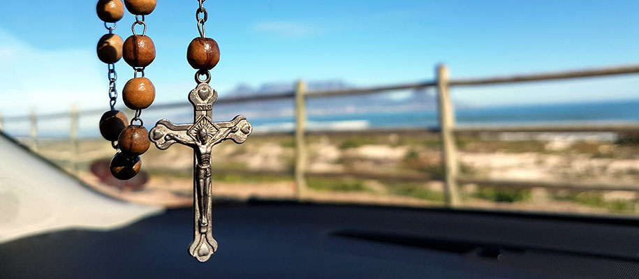 Wooden Rosary beads, cross hanging in frame with blurry outdoor fence behind