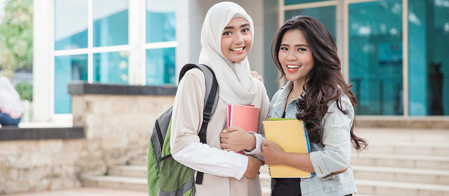 Woman in White hijab and woman with long hair in front of glass campus building