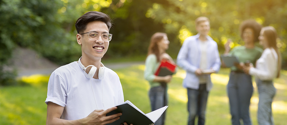 Asian man with glasses and headphones smiling, four people grouped out of focus