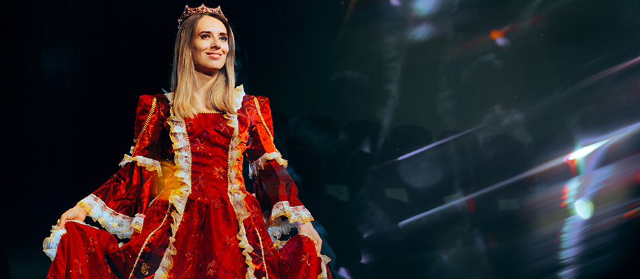 White woman in crown and red historical dress on stage with streaking lights