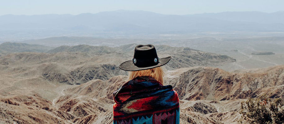 Back of blond person with cowboy hat and poncho looking over desert mountains