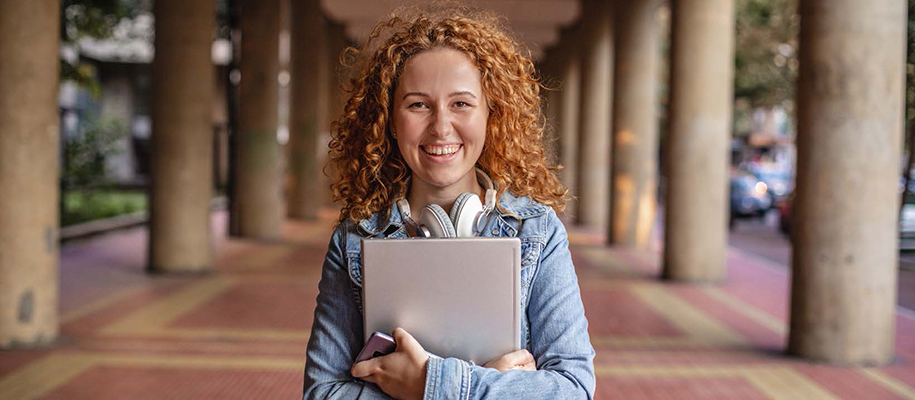 White woman with curly red hair wearing headphone around neck, holding notebook