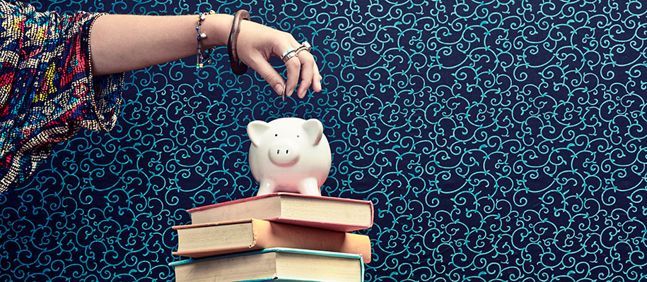 Woman's hand dropping coin into piggy bank atop books with festive background