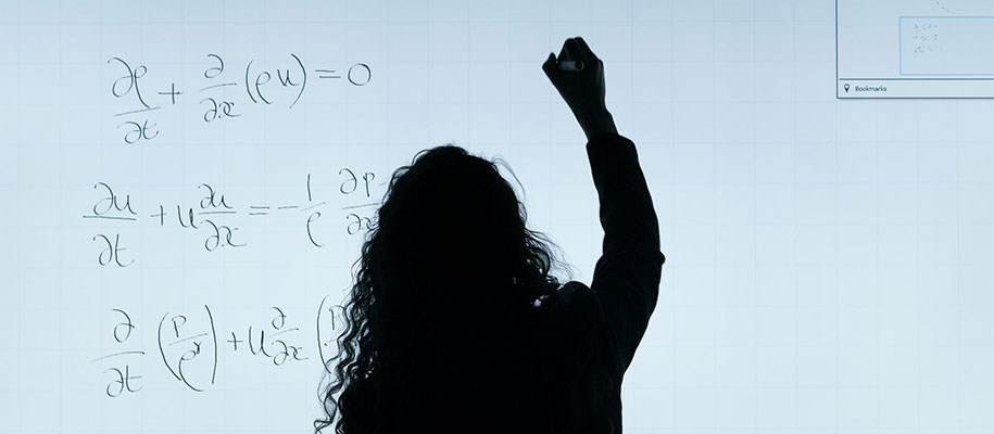 Silhouette of long curly haired woman writing formulas on a whiteboard