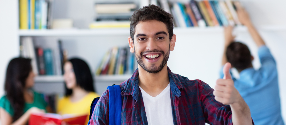 Hispanic man with beard smiling and giving thumbs up in library