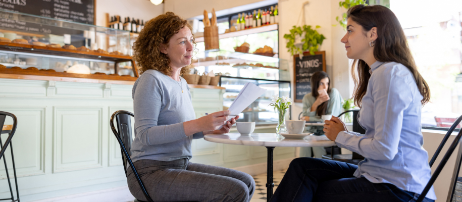 Older White woman with papers, interviewing young white woman in coffee shop