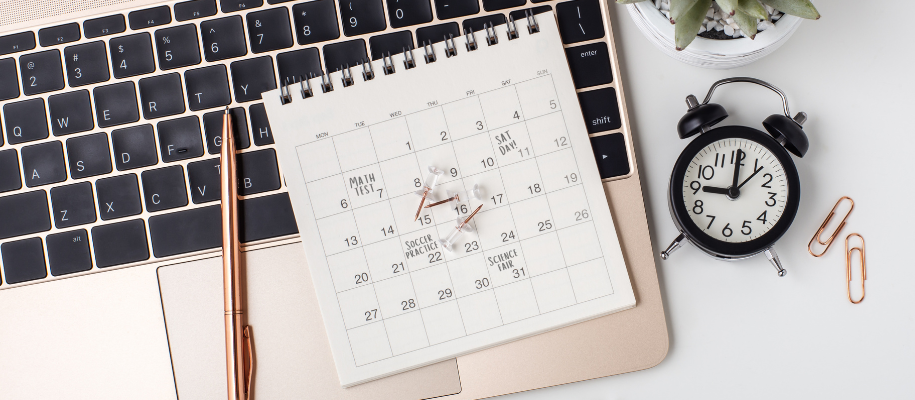 Calendar with student schedule dates on laptop keyboard with pen and clock