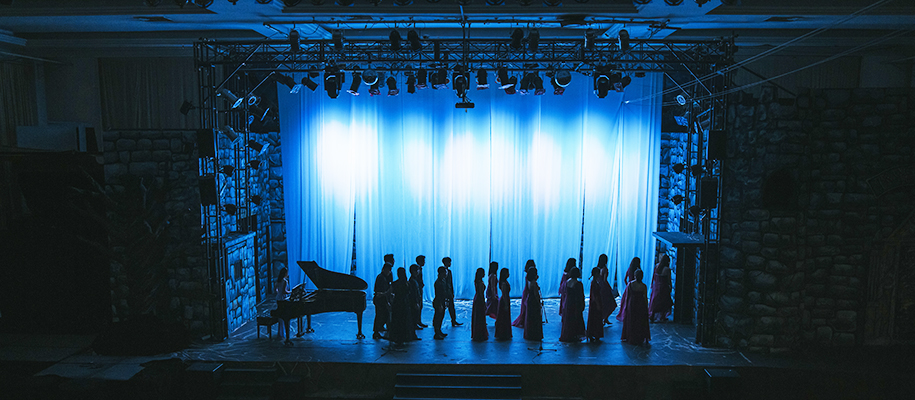 Theater stage in dim blue lighting with choir group readying to perform