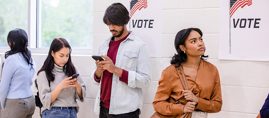 Three young diverse people standing in line to vote, two looking down at phones