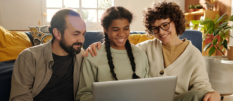 Diverse multi-racial family of three, smiling and looking at laptop
