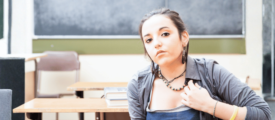 Young woman at a desk in a classroom with a questioning expression