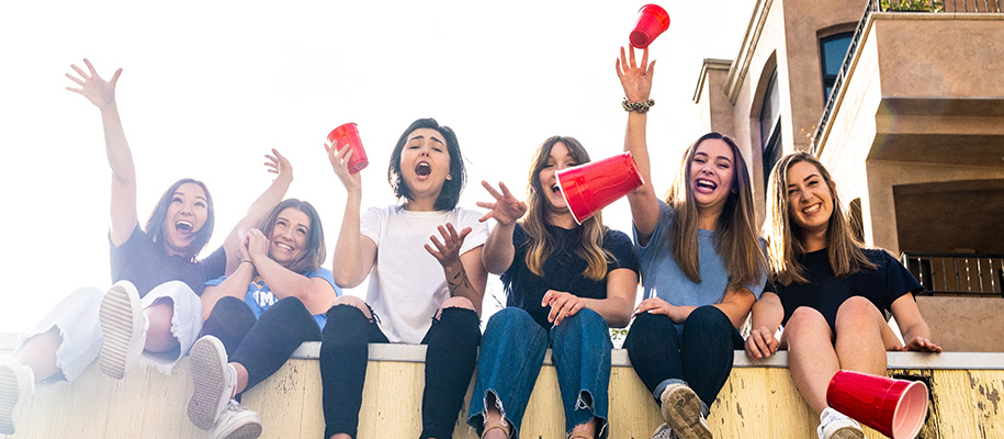 Group of college women sitting on wall throwing red solo cups at camera