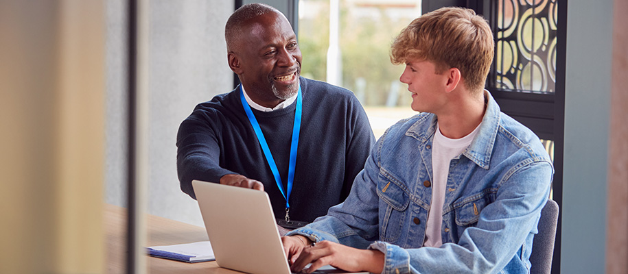 Black counselor in blue sweater with White male student working on laptop