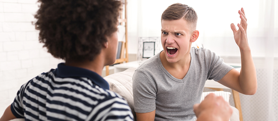 White man in gray shirt and Black man having argument on couch in dorm