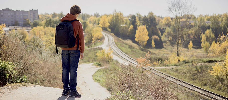 White man with backpack standing back to camera overlooking traintracks