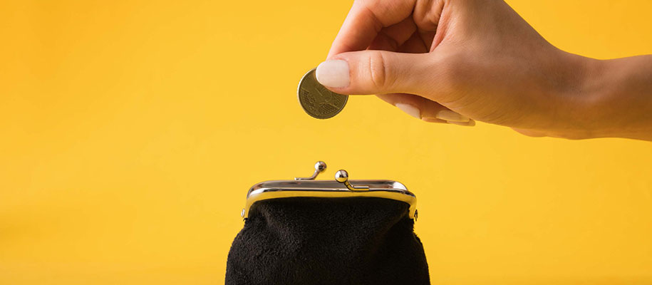 White female hand putting coin into black coin purse against yellow backdrop