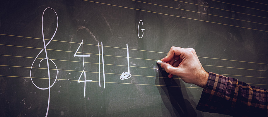 Arm of White person in plaid shirt writing music notes in chalk on lined board