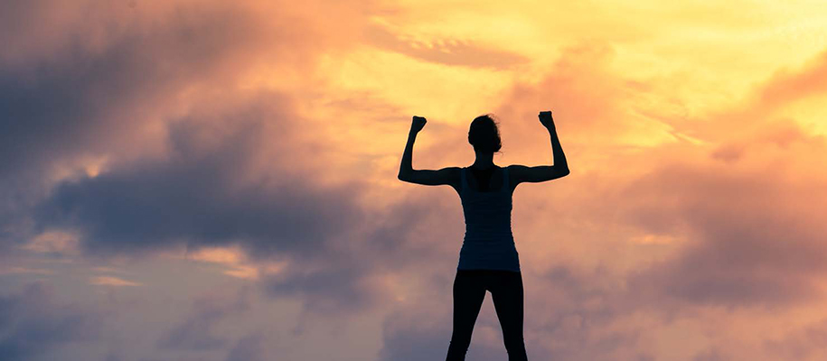 Silhouette of woman flexing muscles up on sunlit dark clouds