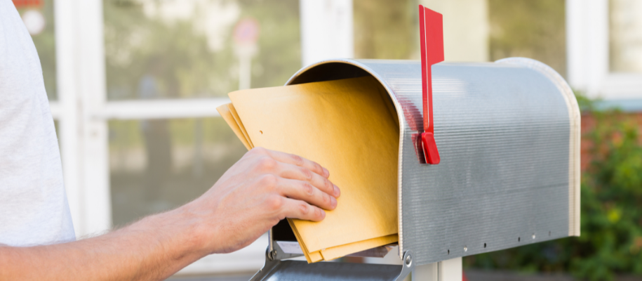 Hand of White person pulling yellow envelopes out of mailbox with flag up