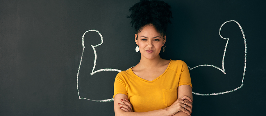 Black woman, yellow shirt crossing arms, chalkboard drawing of flexing muscles
