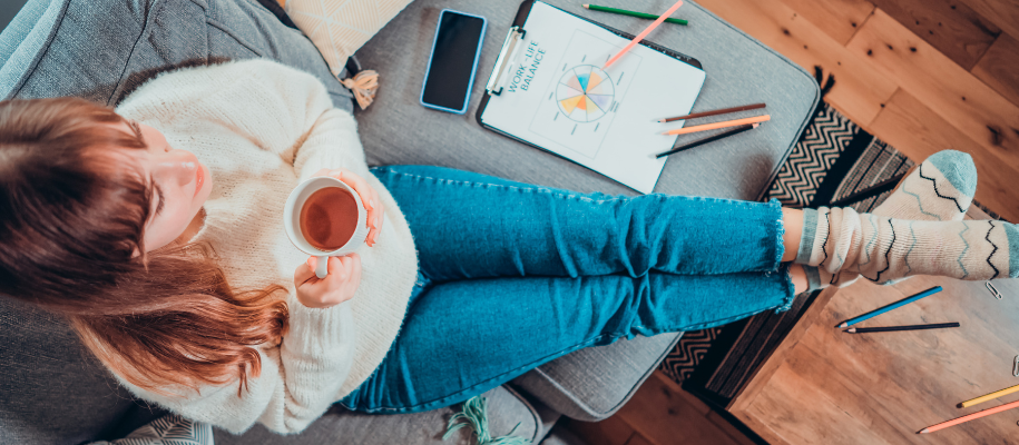 White woman in sweater with tea, relaxing on couch with work-life balance sheet