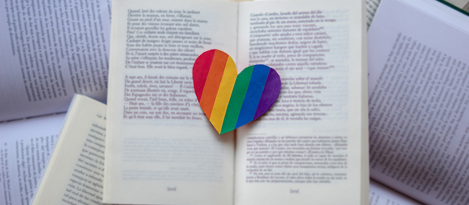 Pile of open books with rainbow heart sitting in the center of the book on top