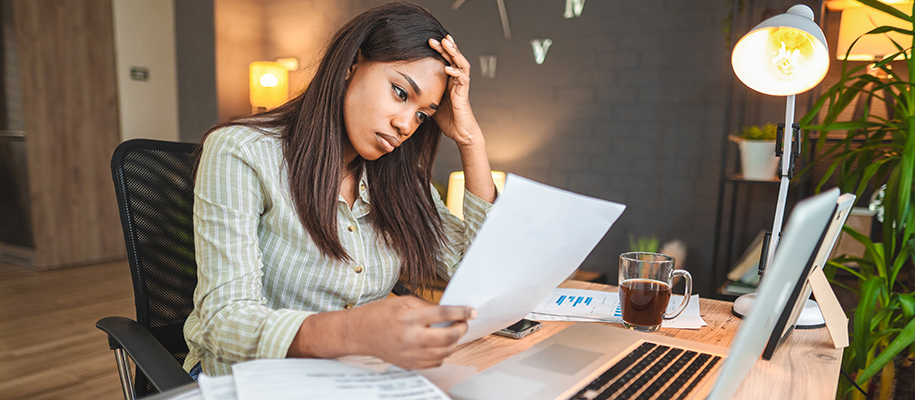 Black woman in green striped shirt at desk looking through financial documents