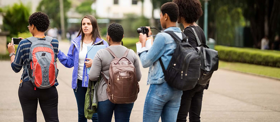 White female tour guide showing four Black students with cameras around campus
