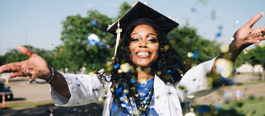 Black woman happily throwing glitter at camera with a graduation cap on