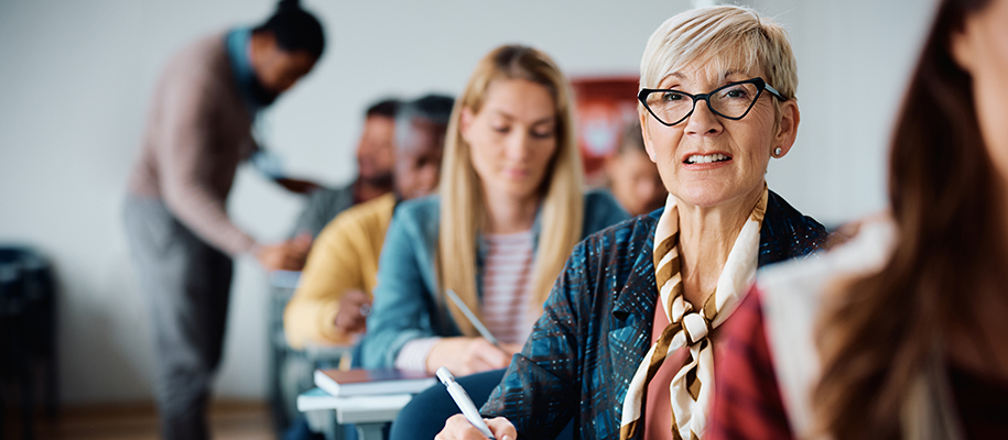 Older White woman with funky glasses in classroom of students, smiling at camera