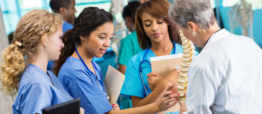 Three diverse women in scrubs looking at spine model held by female doctor
