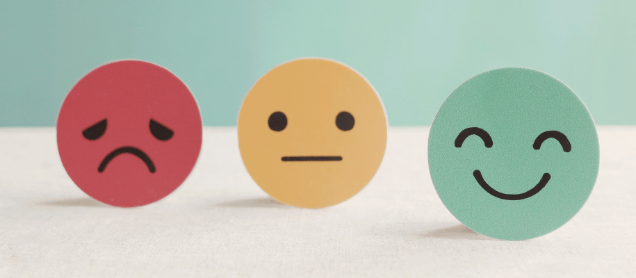 Paper cutouts: a red frowning face; yellow straight face; green smilie face