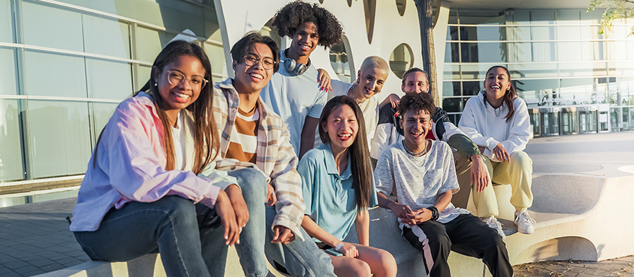 Group of eight diverse students smiling on sunny campus bench