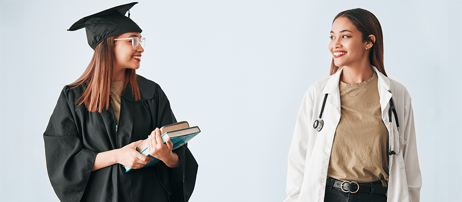 Black woman in black grad robe with books looking at herself in doctor's coat