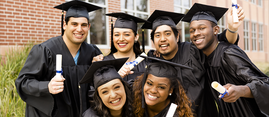 Group of diverse POC students in black grad caps and gowns holding up diplomas