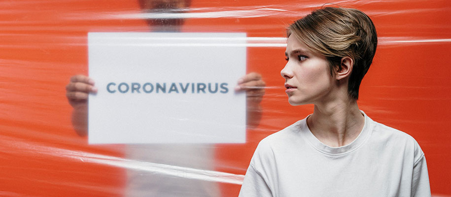 Girl looking sideways through plastic with man holding sign reading coronavirus
