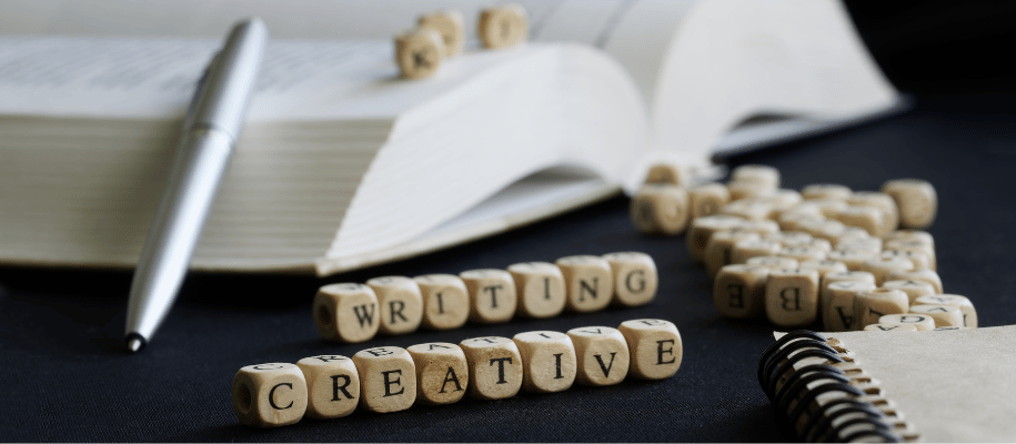 Wooden letters spell "writing" and "creative" in front of a large opened book