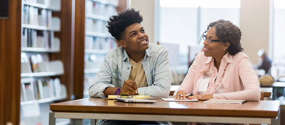 Black teen in button up shirt pondering essay with Black woman counselor in pink