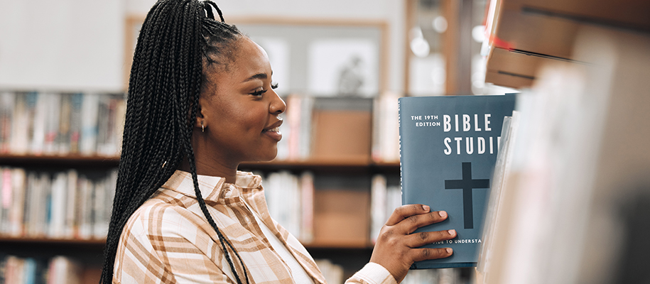 Black woman in brown plaid shirt taking Bible Studies book off library shelf