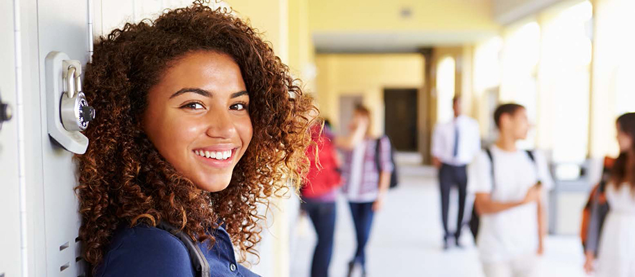 Black girl with curly hair leaning against lockers, smiling at camera