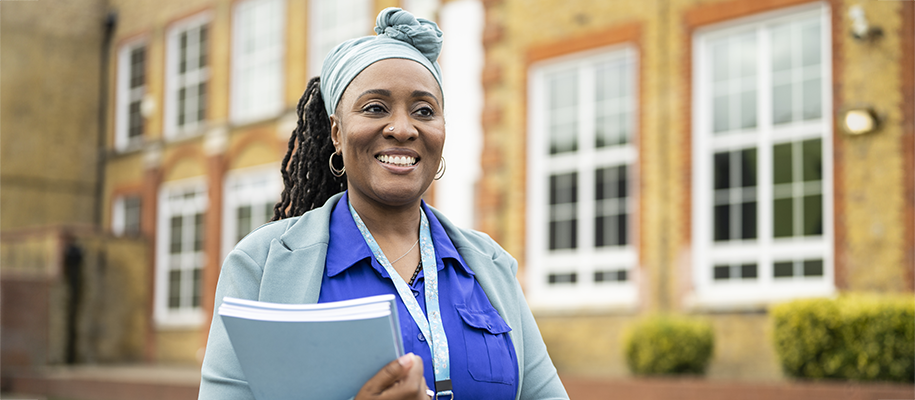 Black woman in blue shirts and headscarf, smiles outside holding papers