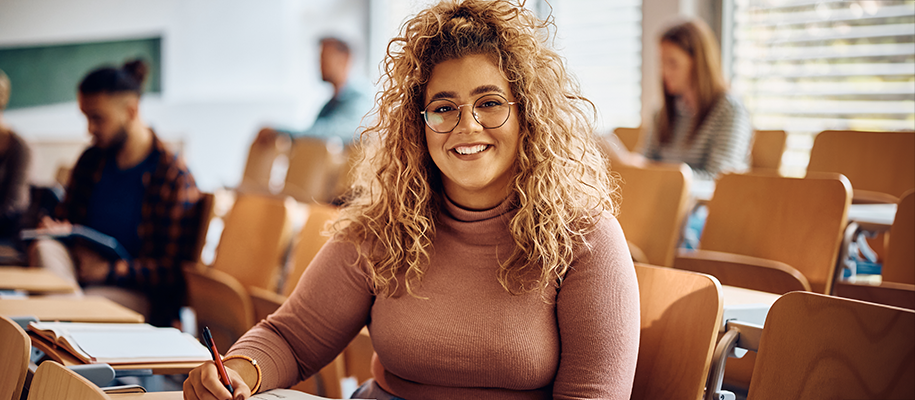 Hispanic woman with curly blond hair smiling at camera in college classroom