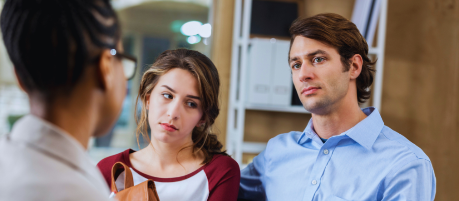 White dad looks frustrated, daughter looks shameful, over shoulder of teacher