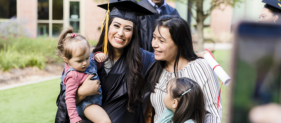 Hispanic woman in grad cap and gown with two young girls and mother, smiling