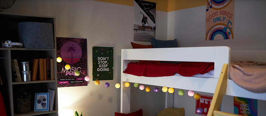 Corner of dorm room with white bunk bed, posters on walls, string lights