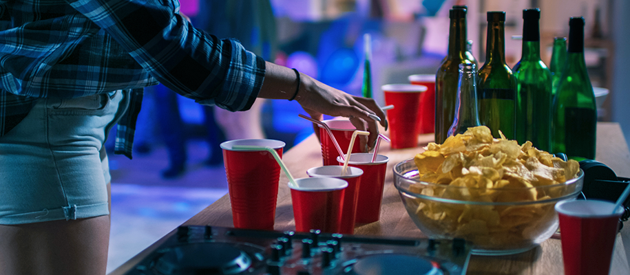 Body of woman in shorts grabbing full red solo cup off table of party drinks