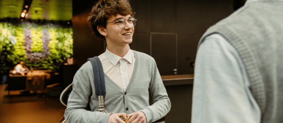 Young man wearing a backpack, smiles at an older man in an office lobby