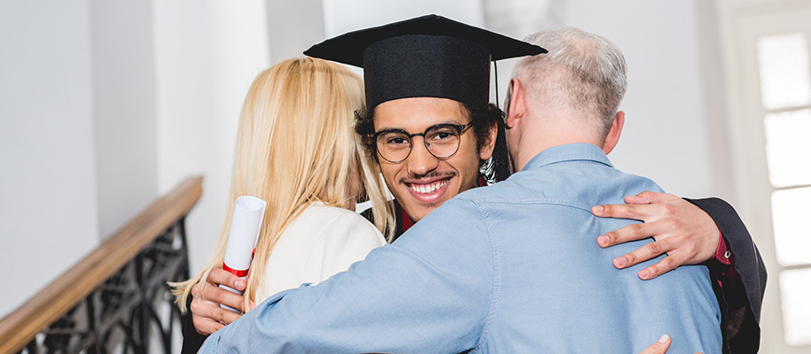 Focus on Black son in black grad cap & gown being embraced by White parents