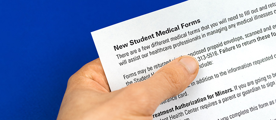 White hand holding new student medical insurance form over dark blue background