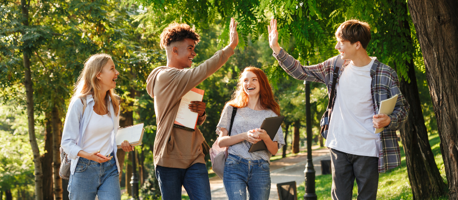 Group of four young students laughing and high-fiving on sunny college campus